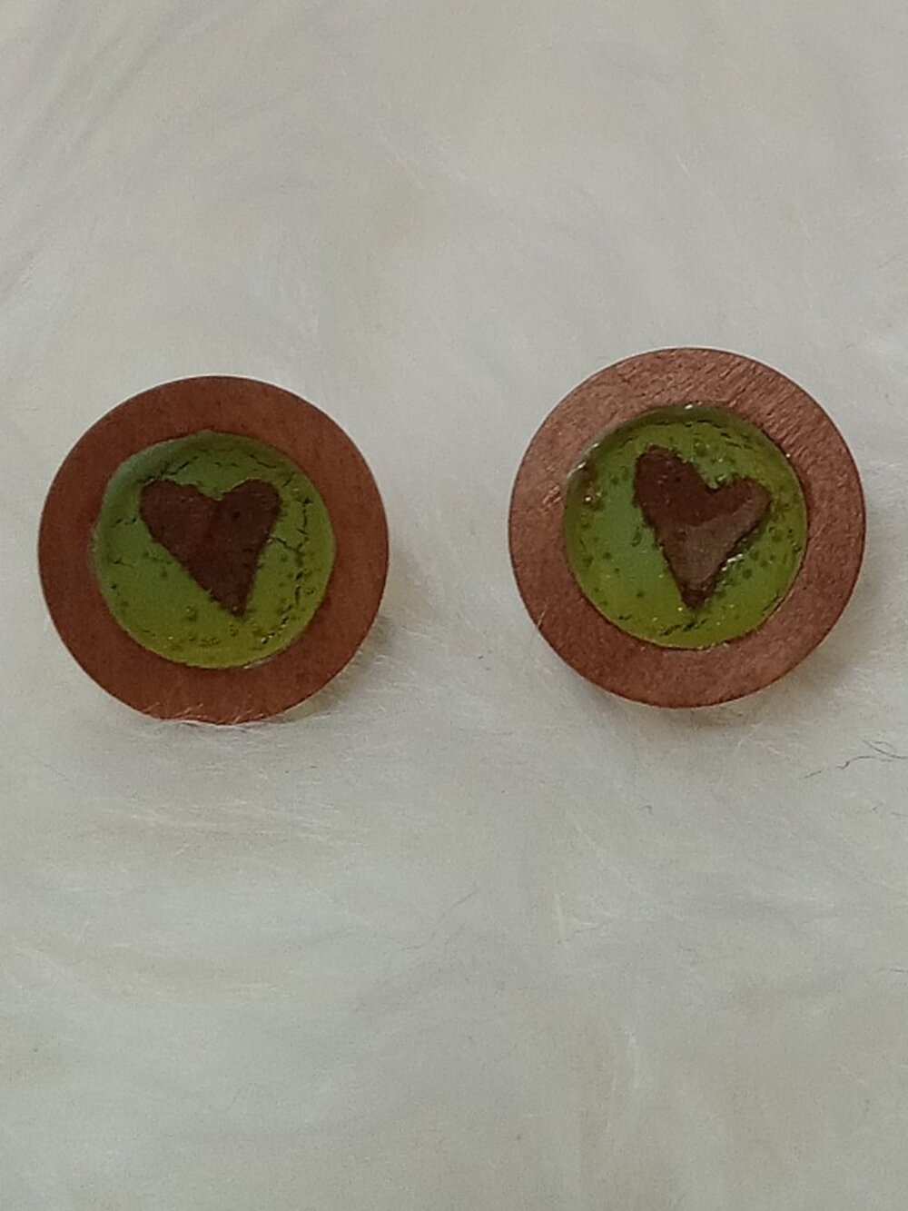 Handmade earrings on a wooden base with a piece of punched-out tree leaf